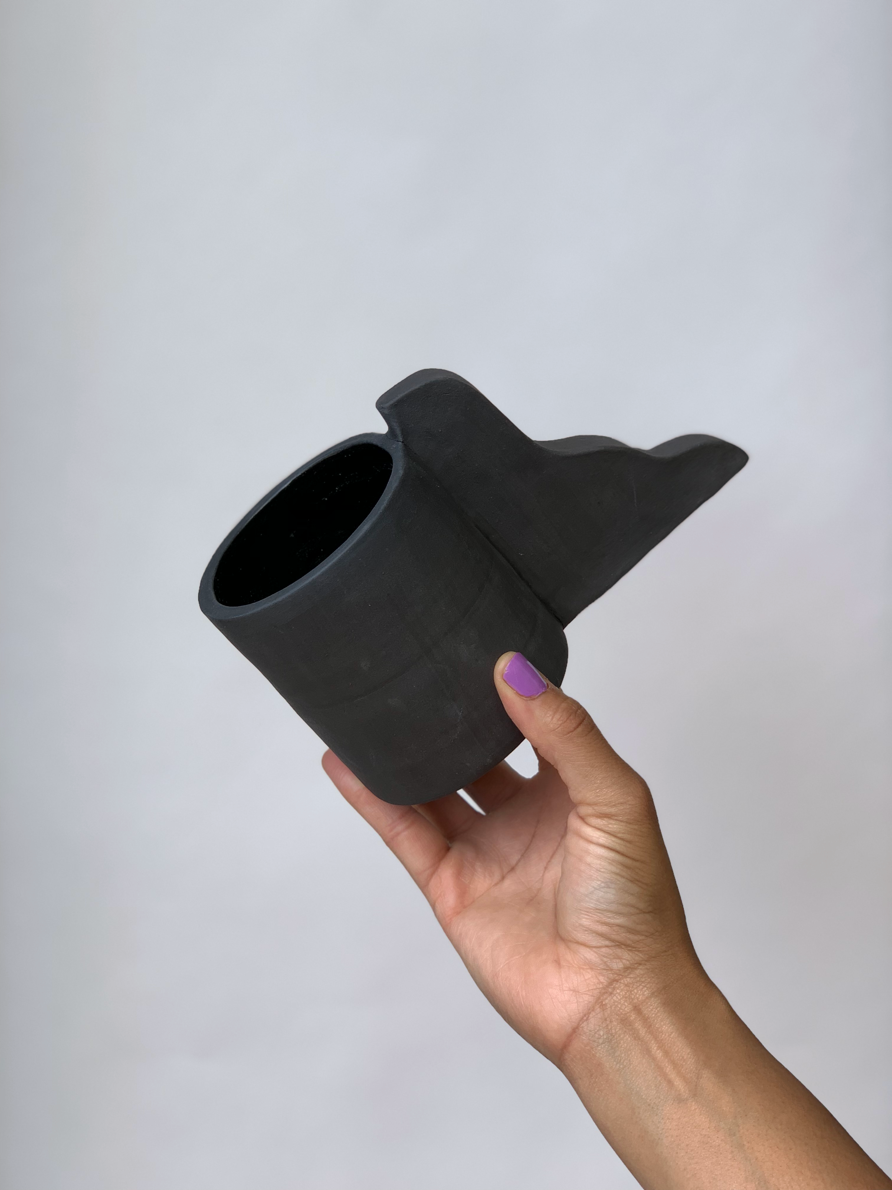 Black matte stoneware ceramic mug with a wavy handle that gets wider at base.