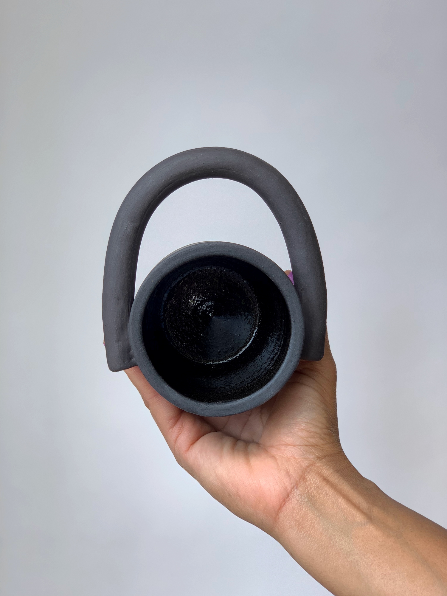 Black matte stoneware ceramic mug with a circular handle extending outwards to the side of the mug as the handle.