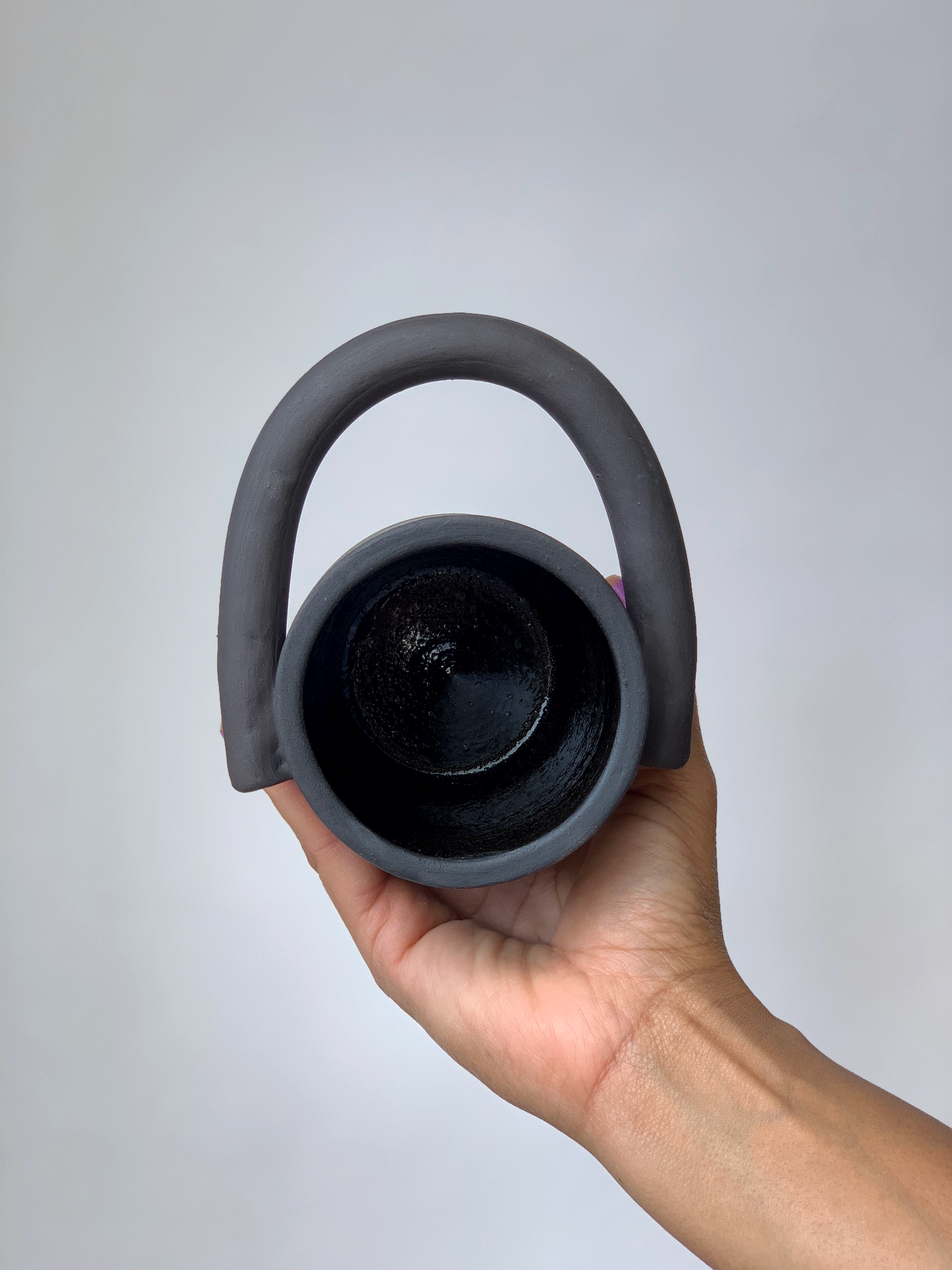 Black matte stoneware ceramic mug with a circular handle extending outwards to the side of the mug as the handle.