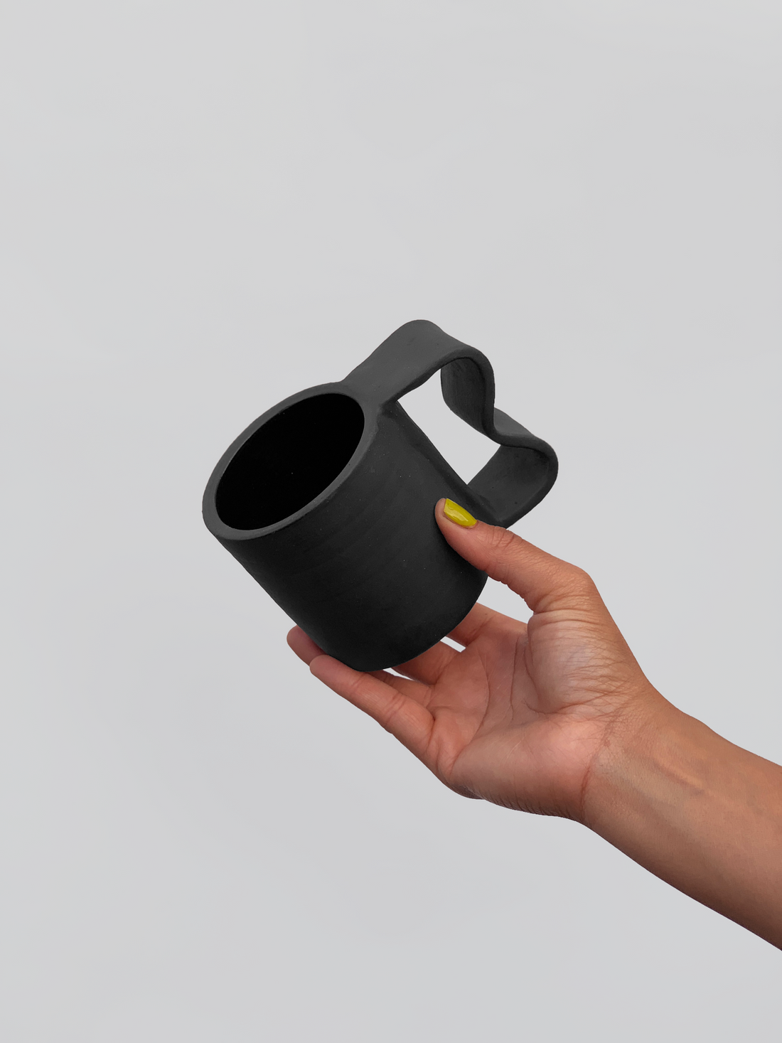 Black matte stoneware ceramic mug with a  wide wavy inlet handle.