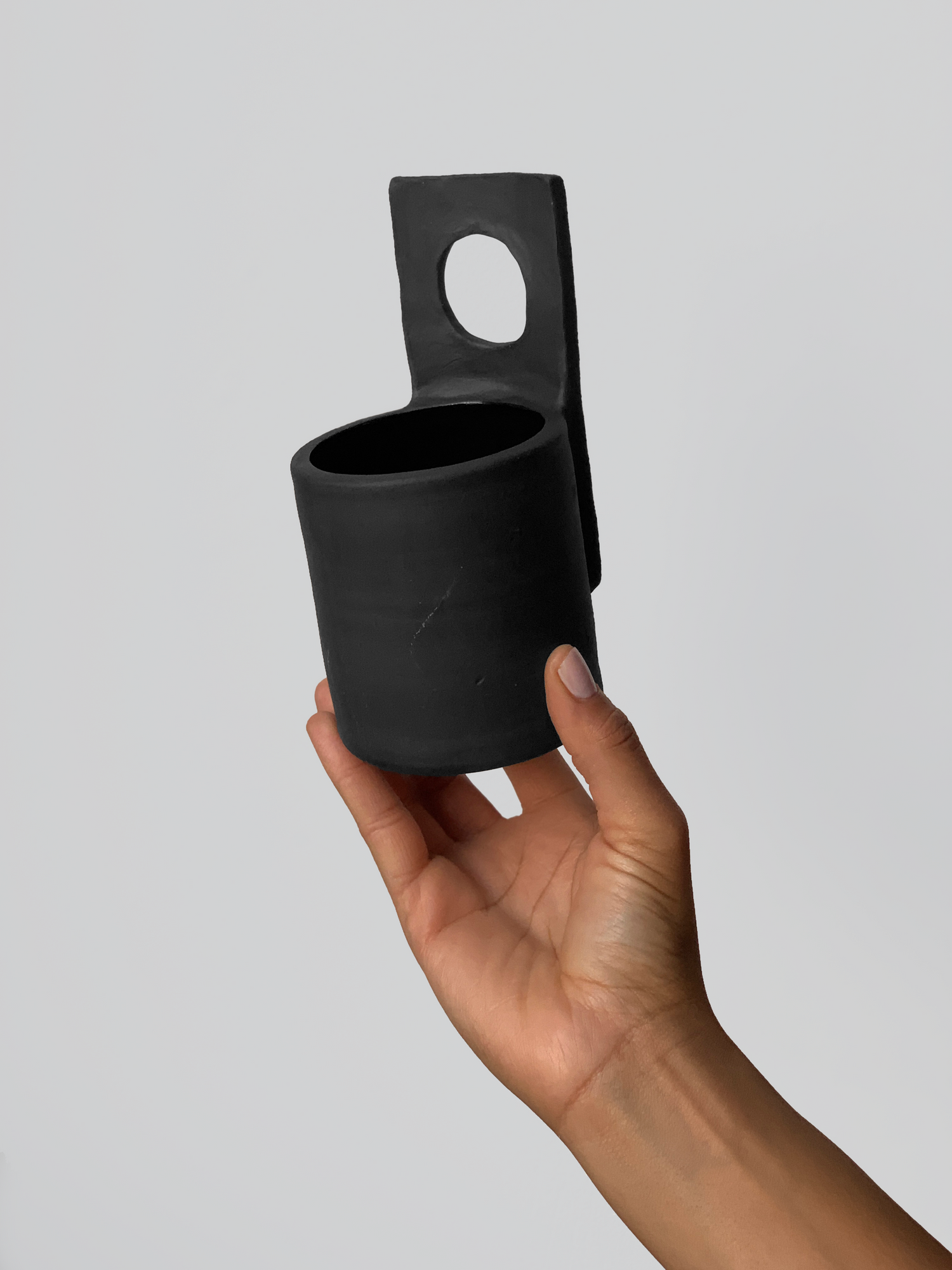 Black matte stoneware ceramic mug with upwards facing flat square circle center as the handle.