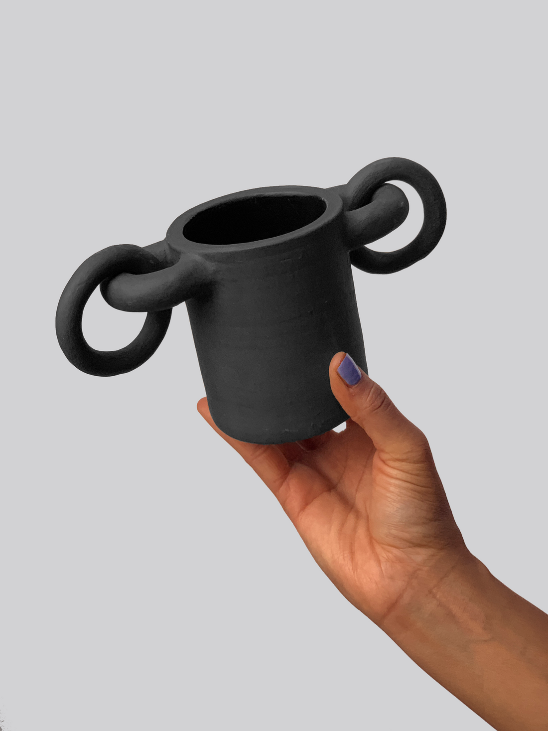 Black matte stoneware ceramic mug with circular shapes on both sides of the mug and rings passing through them as the handle.