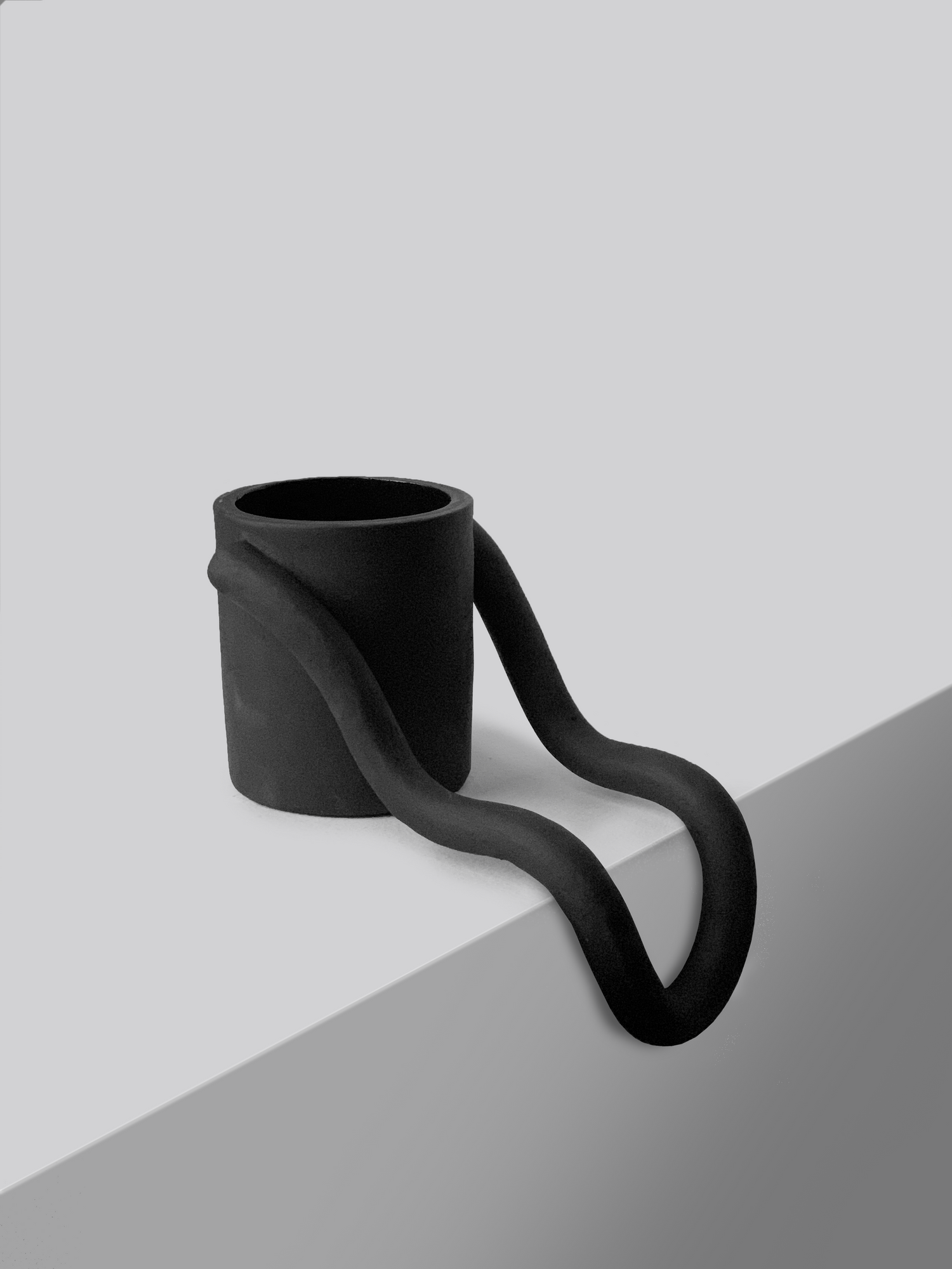 Black matte stoneware ceramic mug with a handle that flows down the side of a surface.