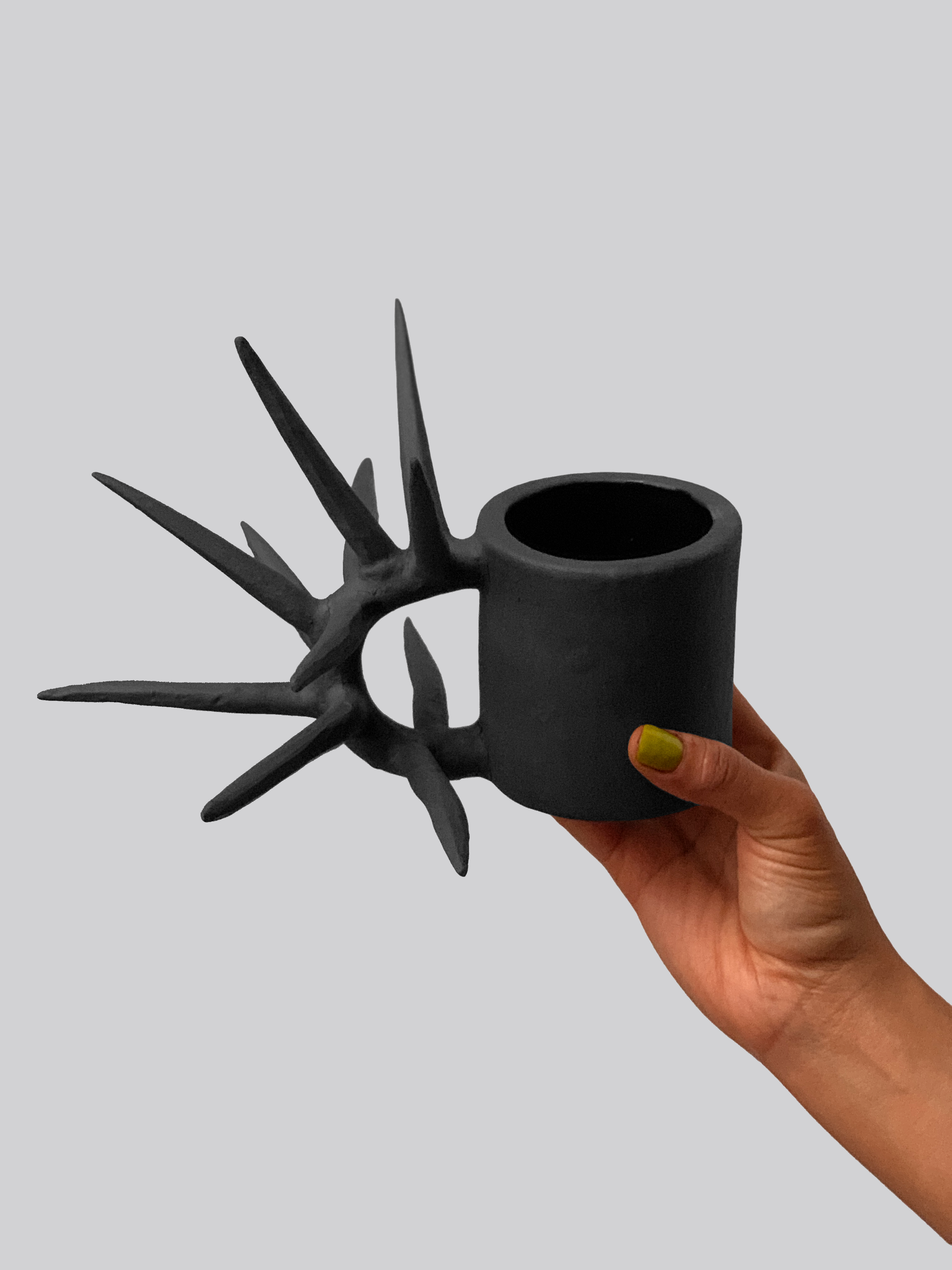 Black matte stoneware ceramic mug with long spikes extending from a circular side handle.