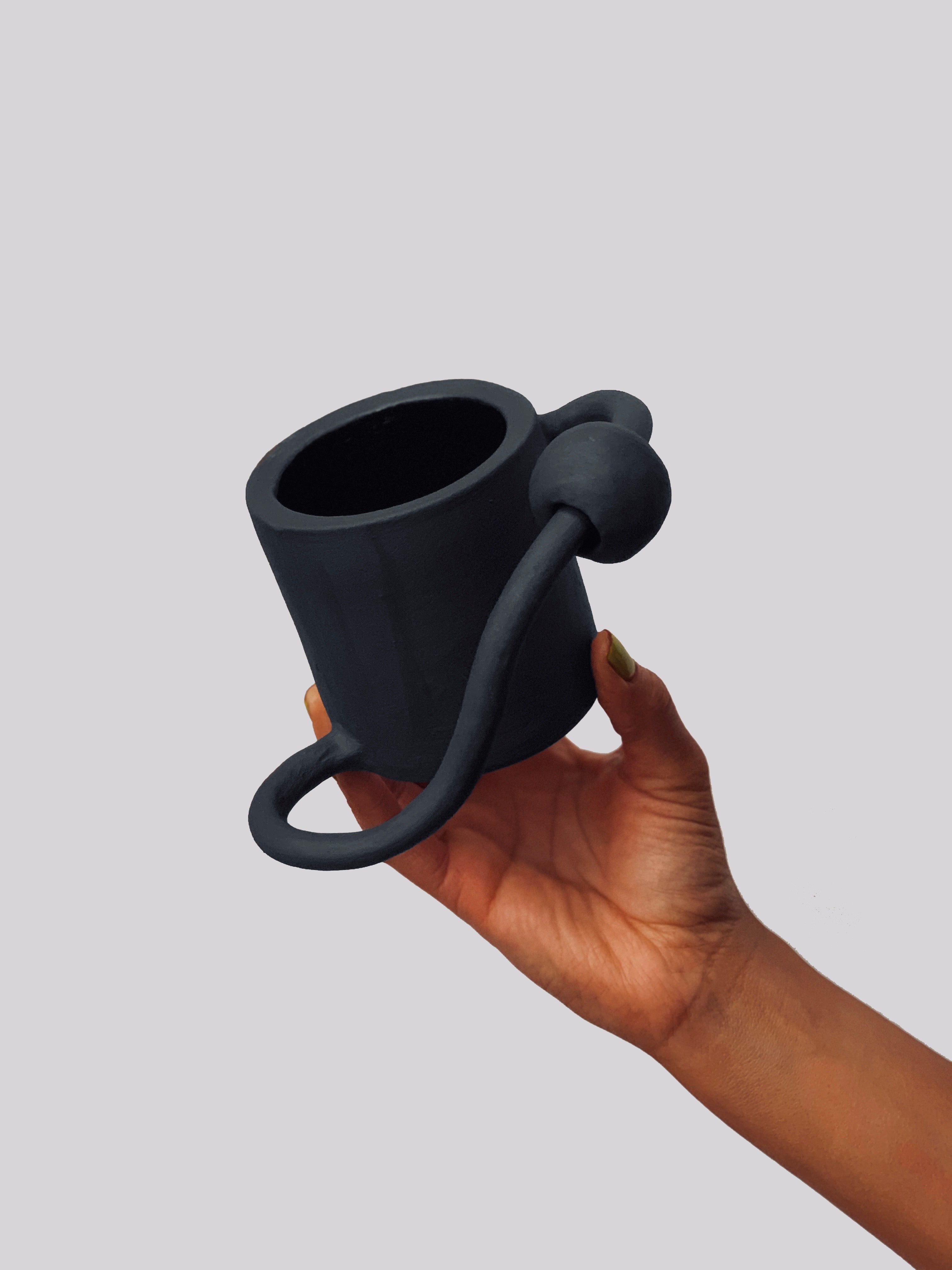 Black matte stoneware ceramic mug with an oval shaped handle on the side of the mug and a ball through the oval shape.