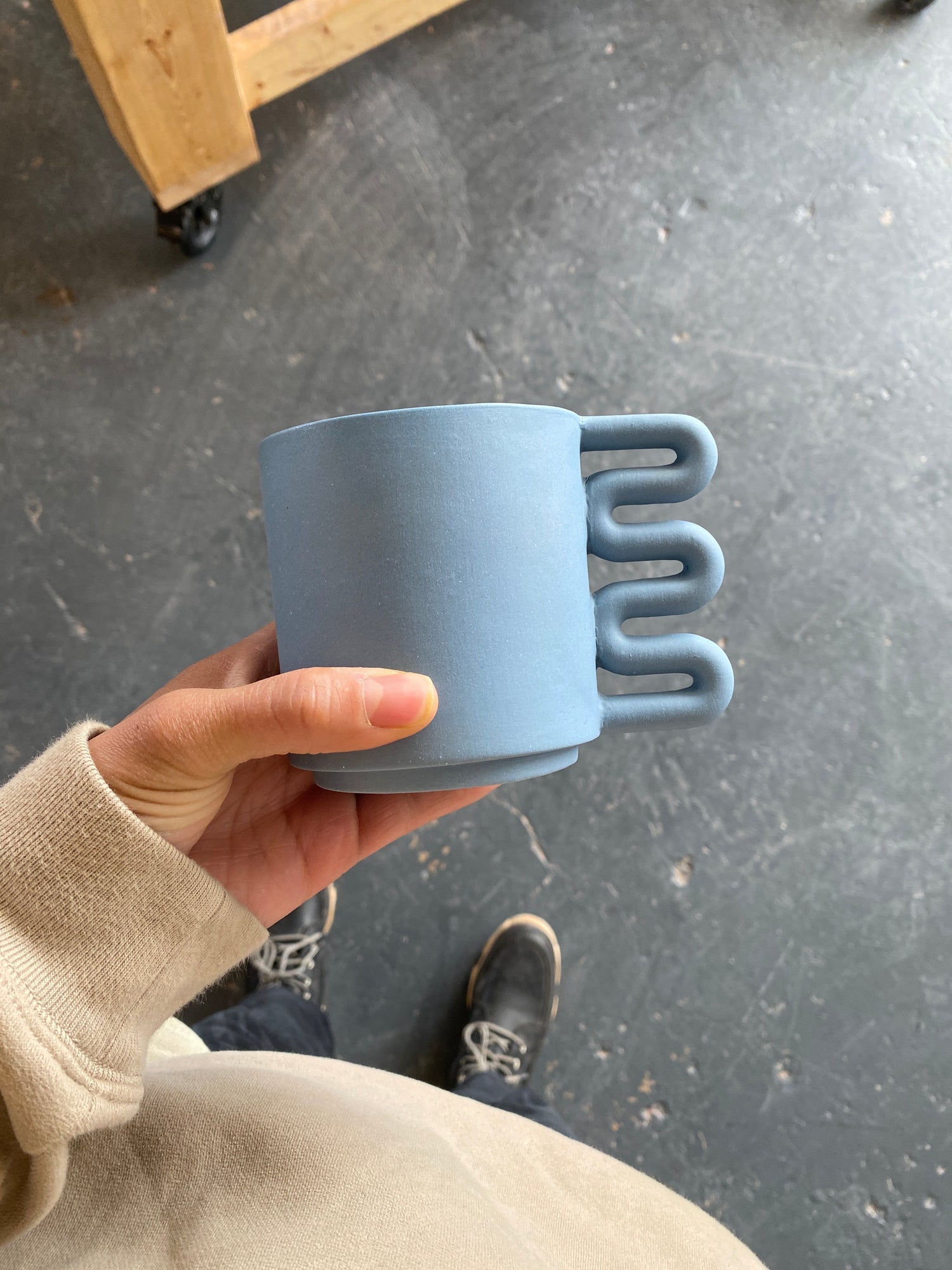 Lolly Ceramics X Merit presents a blue matte stoneware ceramic mug with a squiggle shaped handle.