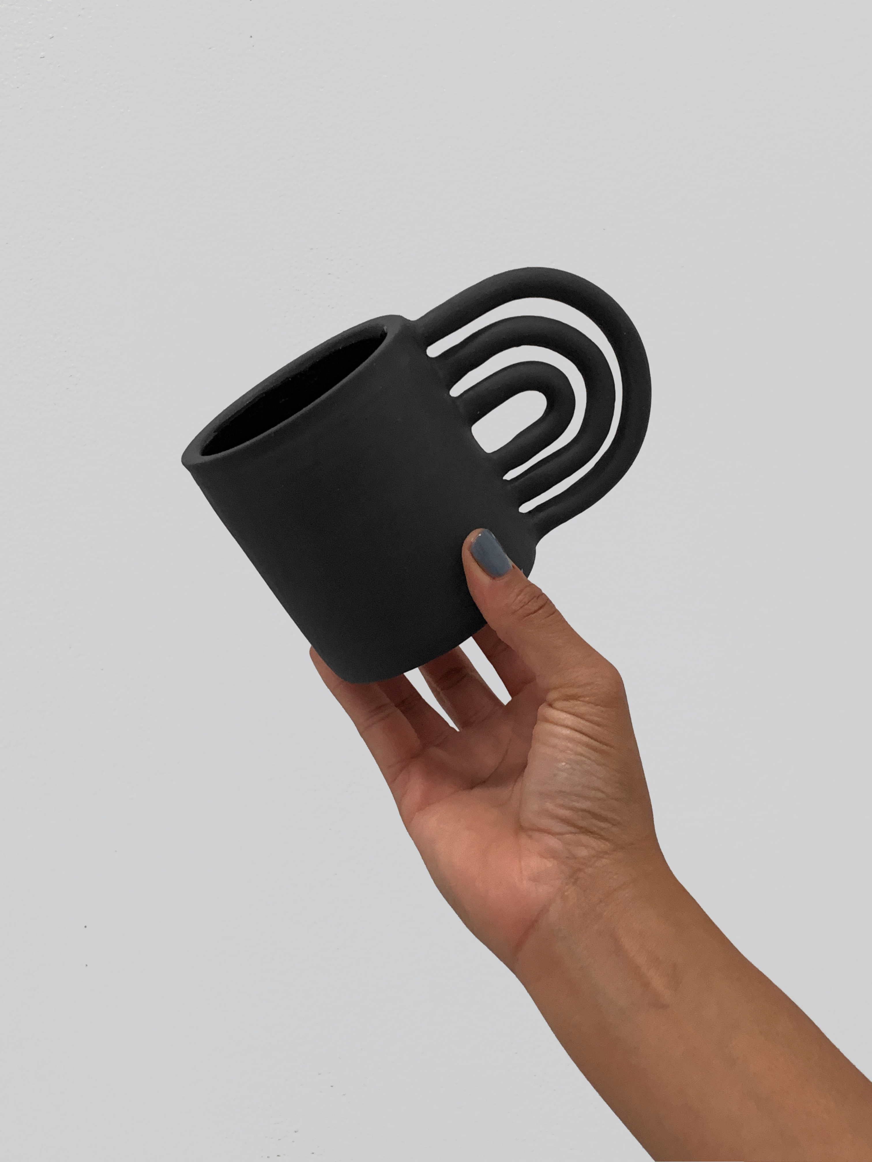Black matte stoneware ceramic mug with a rainbow shaped handle.