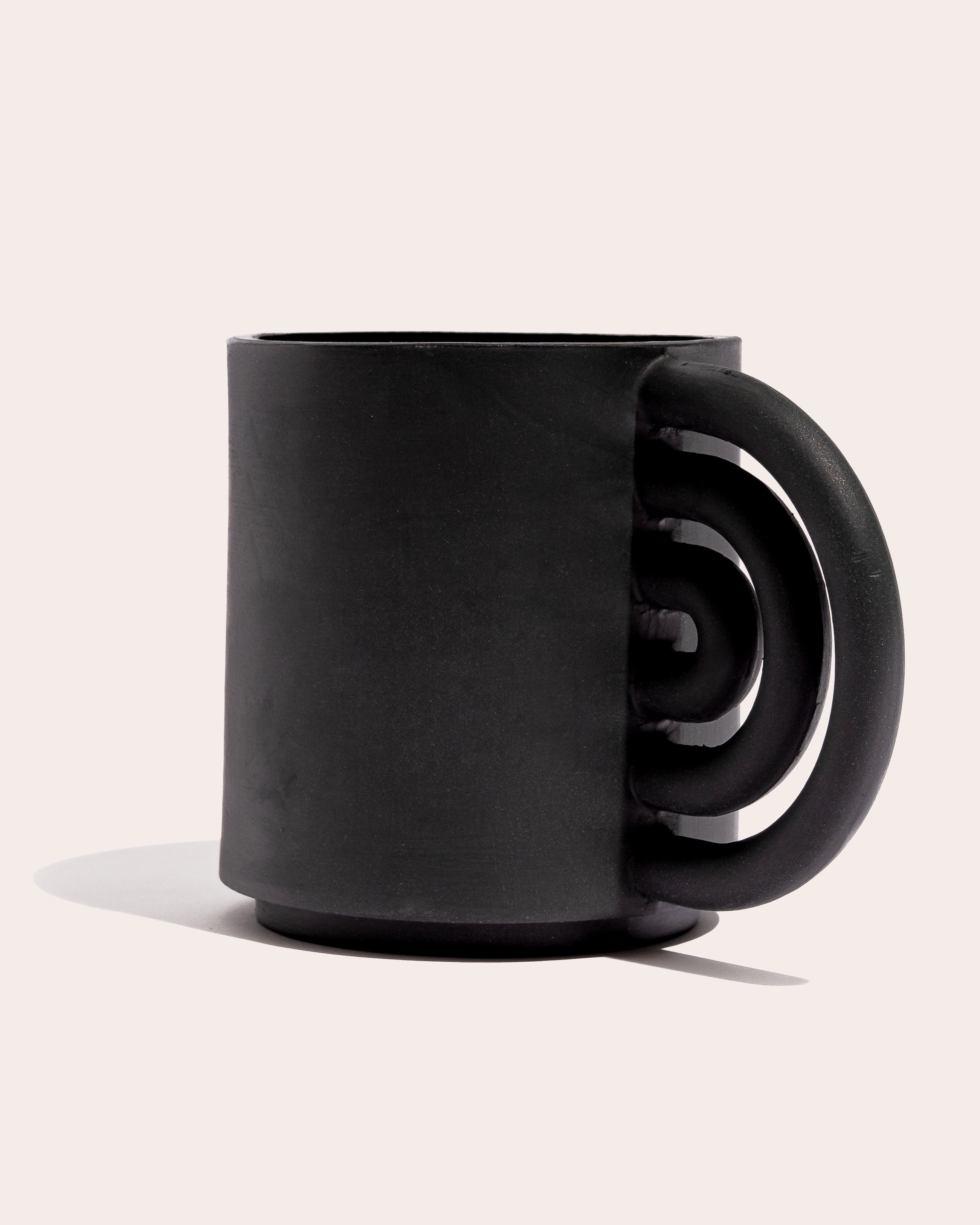 Black matte stoneware ceramic mug with a rainbow shaped handle.