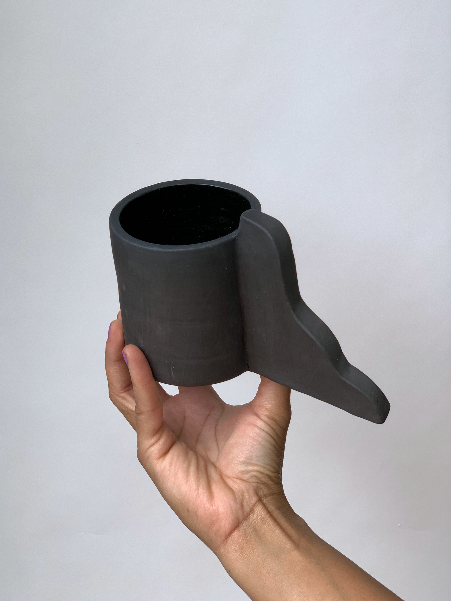 Black matte stoneware ceramic mug with a wavy handle that gets wider at base.