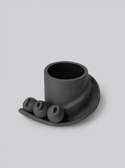 Black matte stoneware ceramic mug with a slide moving down the side of the mug as a handle and three detachable ornamental balls. 