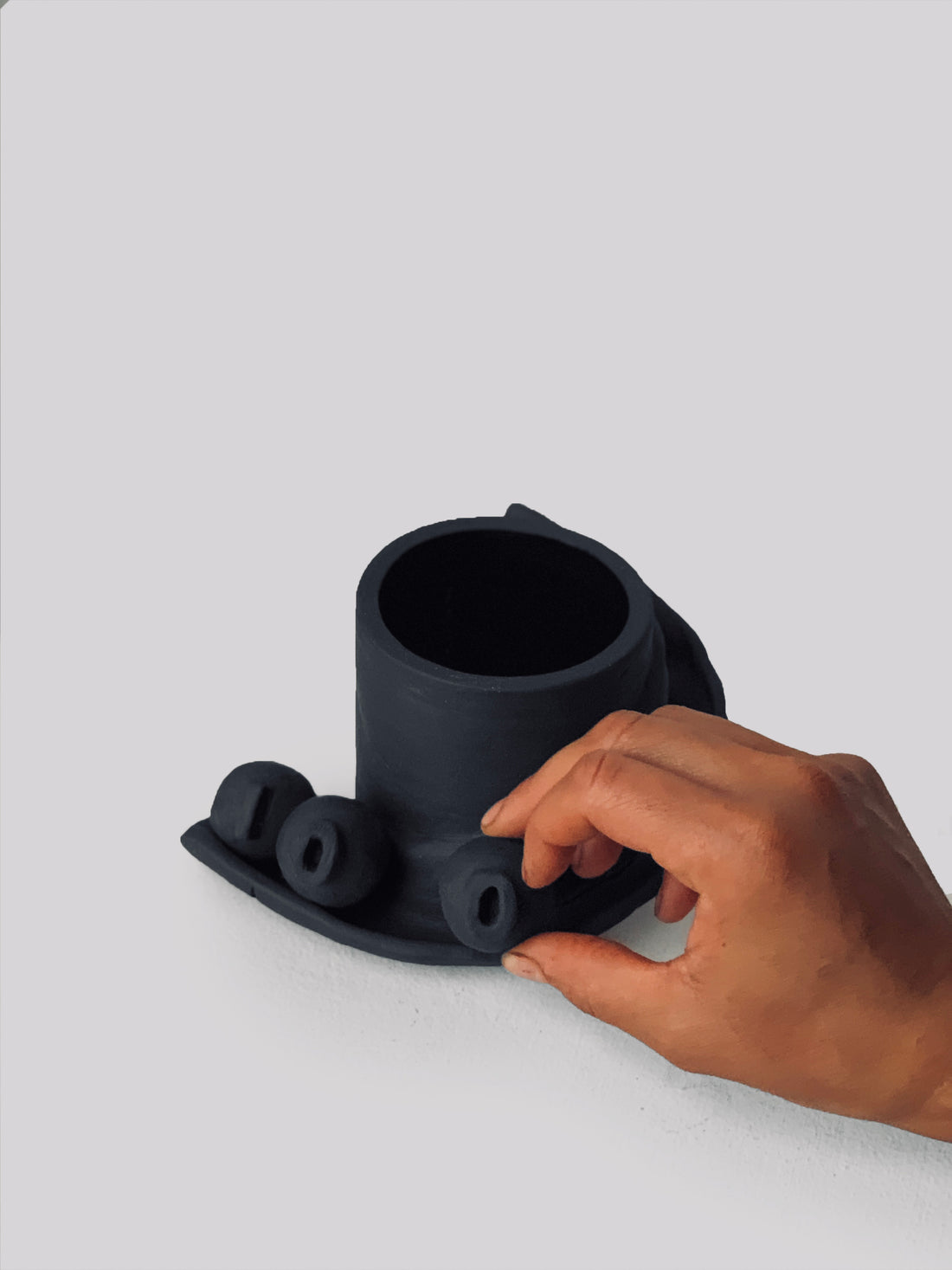 Black matte stoneware ceramic mug with a slide moving down the side of the mug as a handle and three detachable ornamental balls.