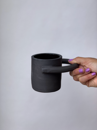 Black matte stoneware ceramic mug with a circular handle extending outwards to the side of the mug as the handle.