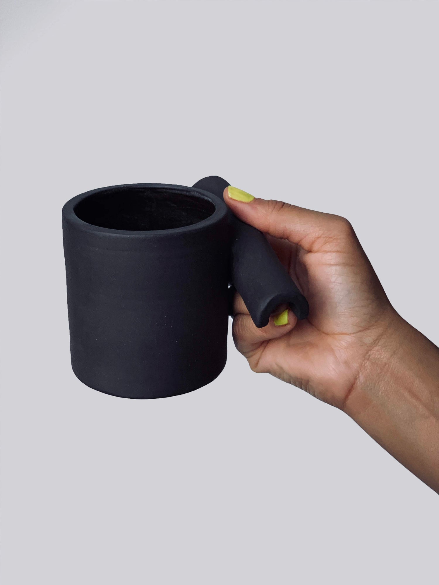 Black matte stoneware ceramic mug with hollow upside down tube handle.