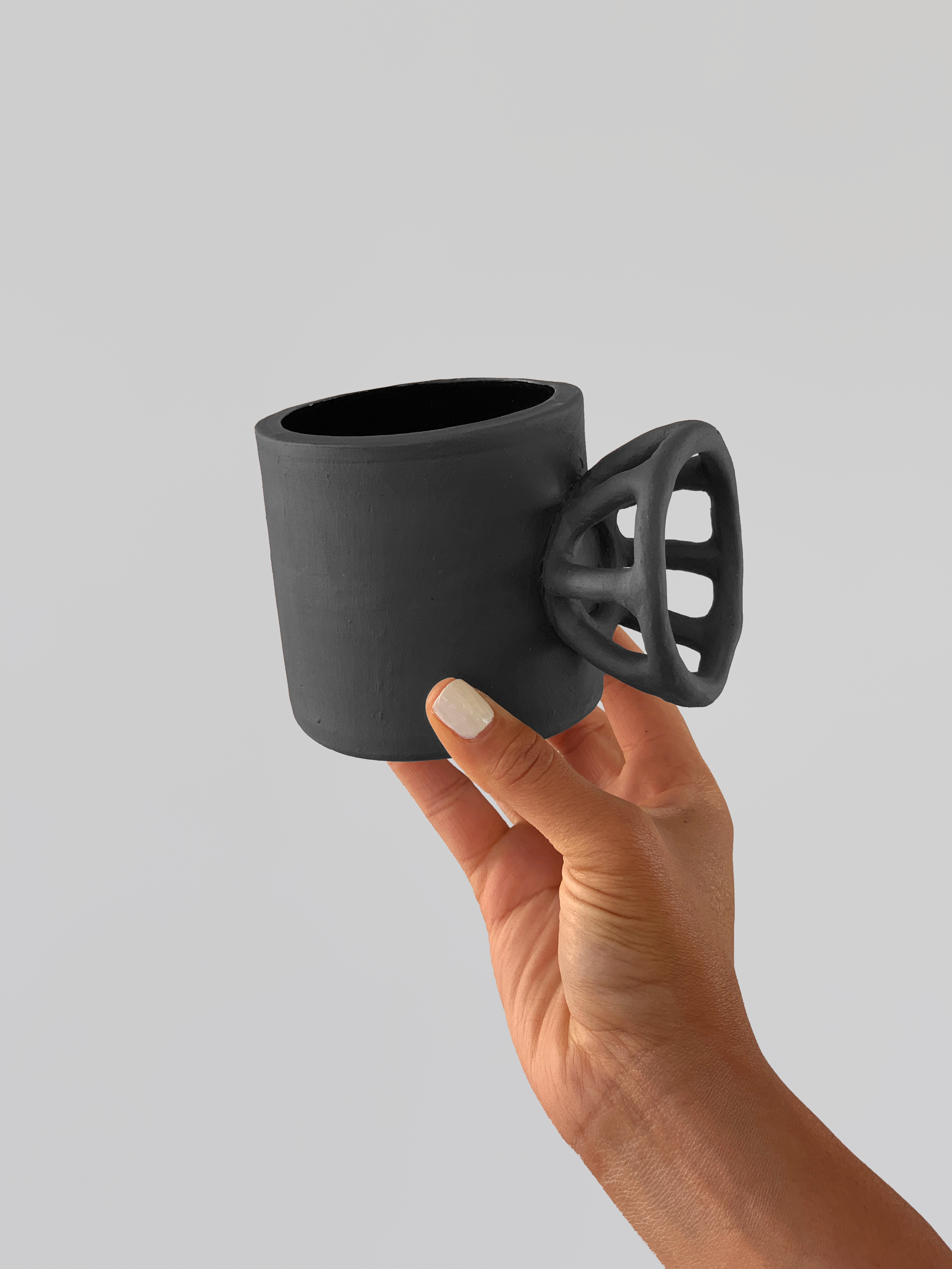 Black matte stoneware ceramic mug with a circular grid knob handle.