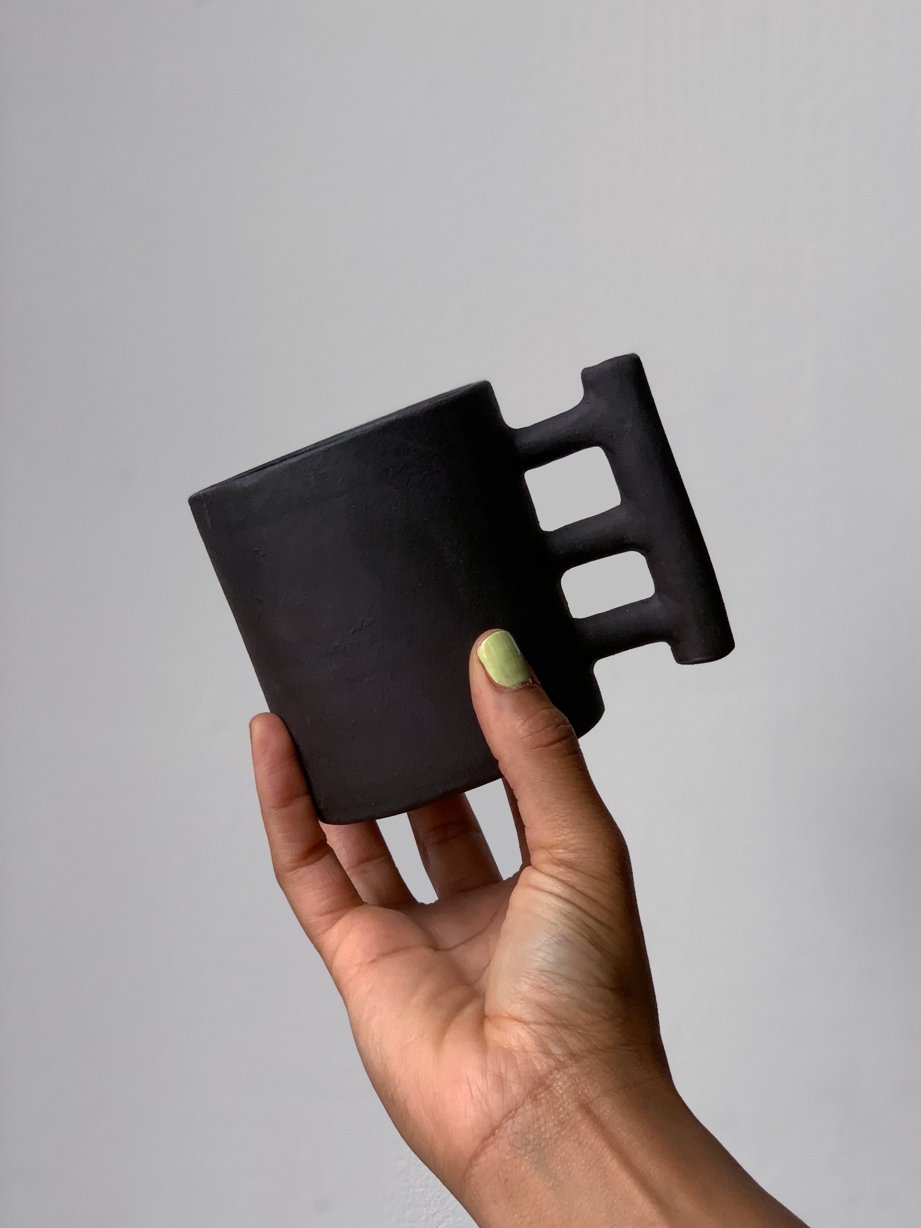 Black matte stoneware ceramic mug with three bars connecting to a thicker bar as the handle.