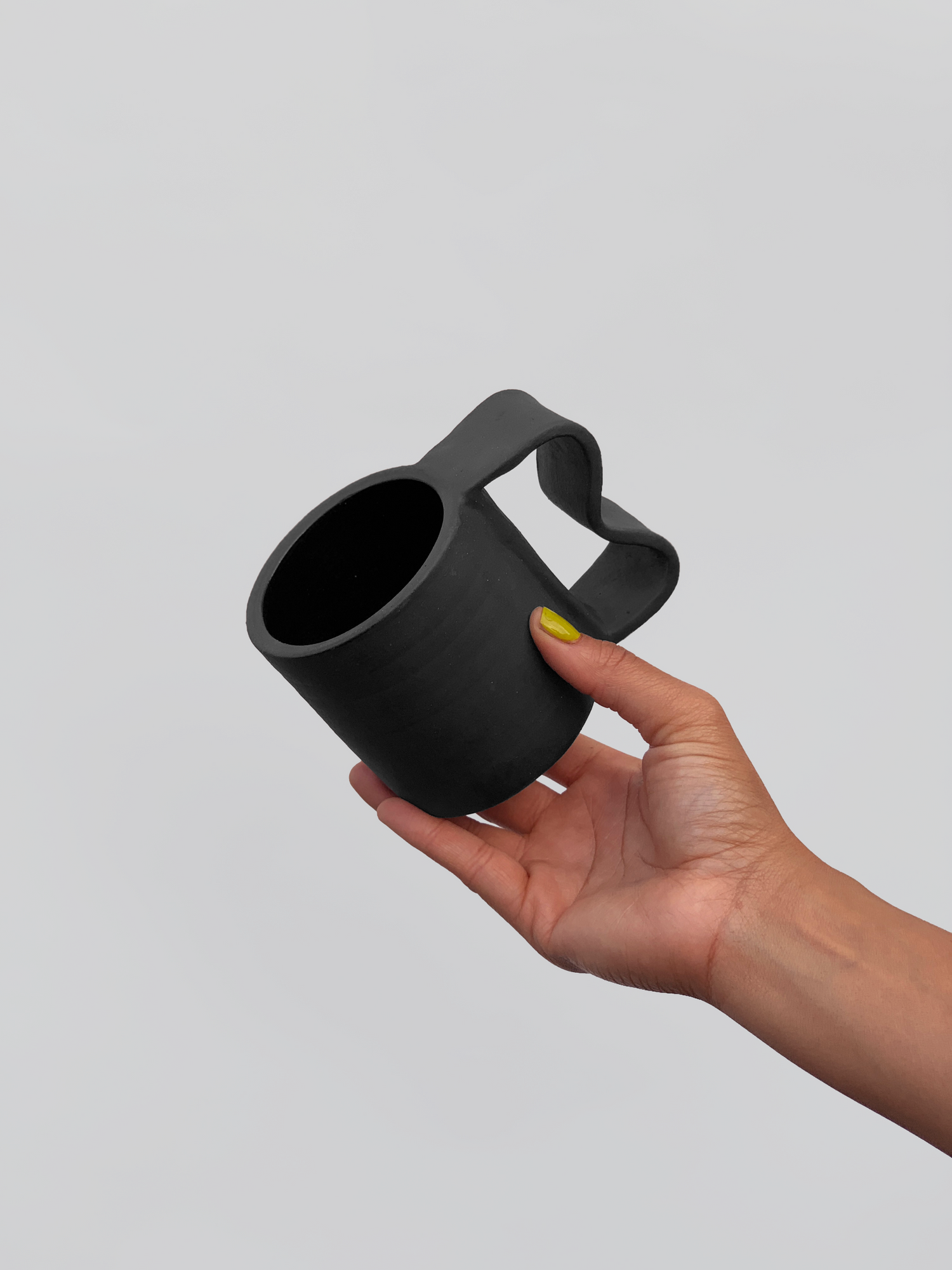 Black matte stoneware ceramic mug with a  wide wavy inlet handle. 