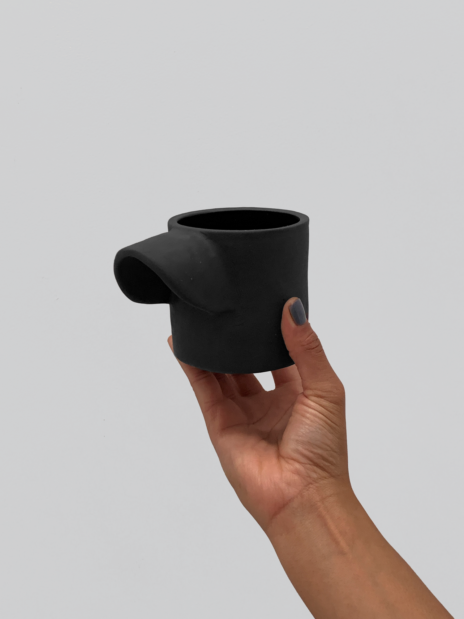Black matte stoneware ceramic mug with an extended inward arching side handle.