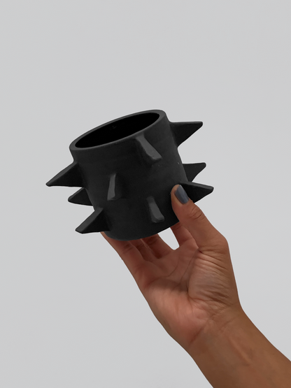 Black matte stoneware ceramic mug with outward facing triangles all throughout the mug as a handle.