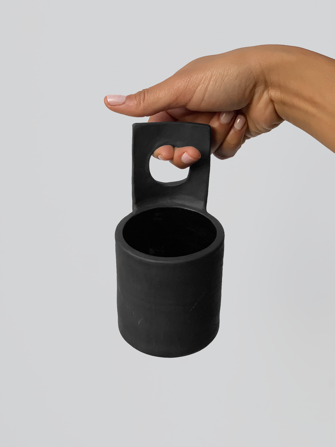 Black matte stoneware ceramic mug with upwards facing flat square circle center as the handle.