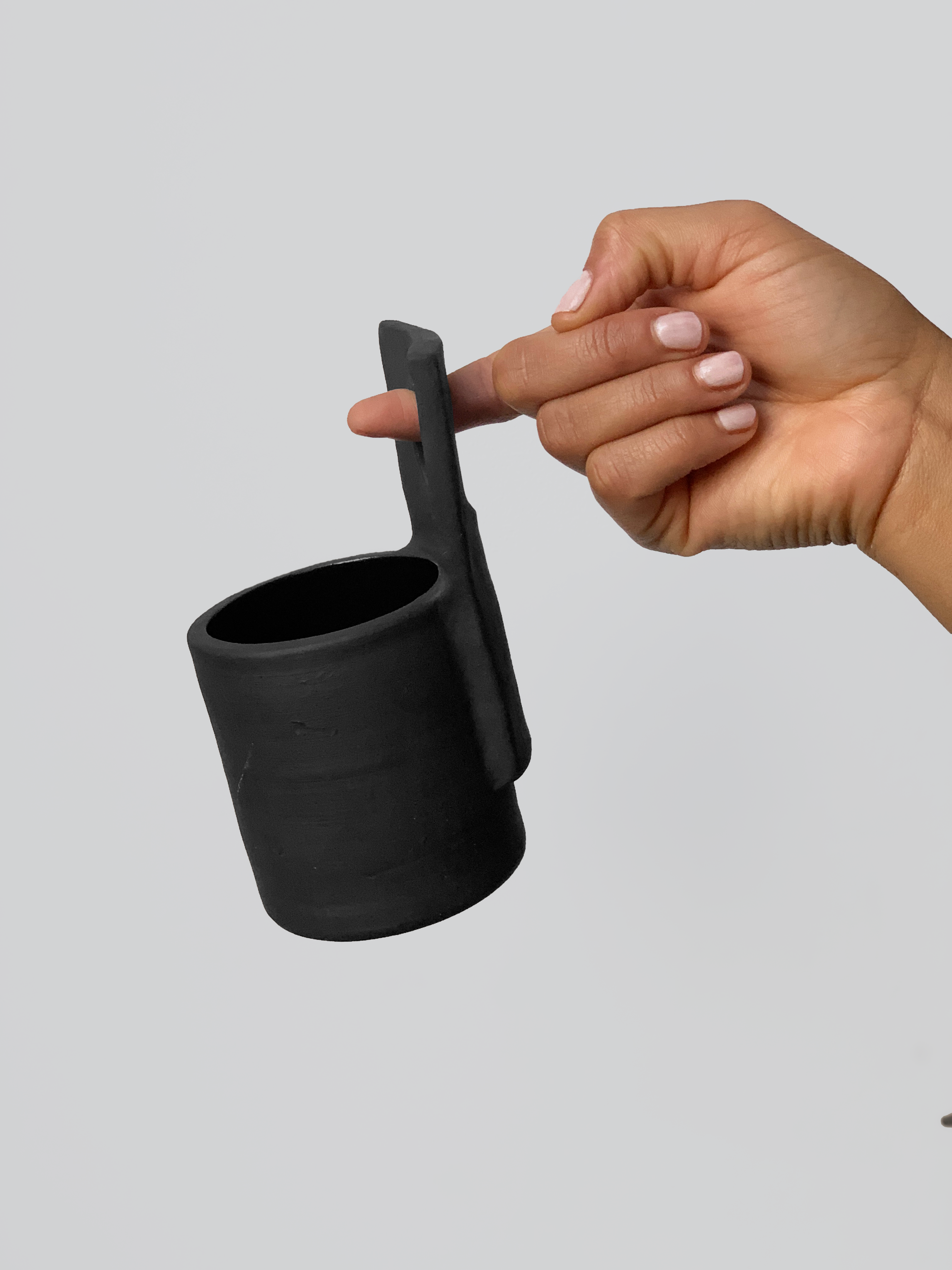 Black matte stoneware ceramic mug with upwards facing flat square circle center as the handle.