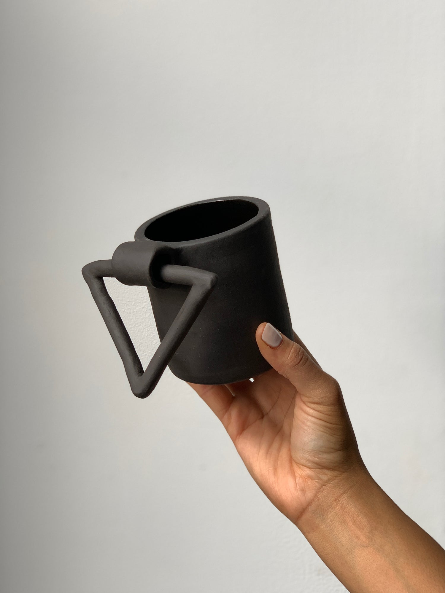 Black matte stoneware ceramic mug with hanging triangle shaped handle.