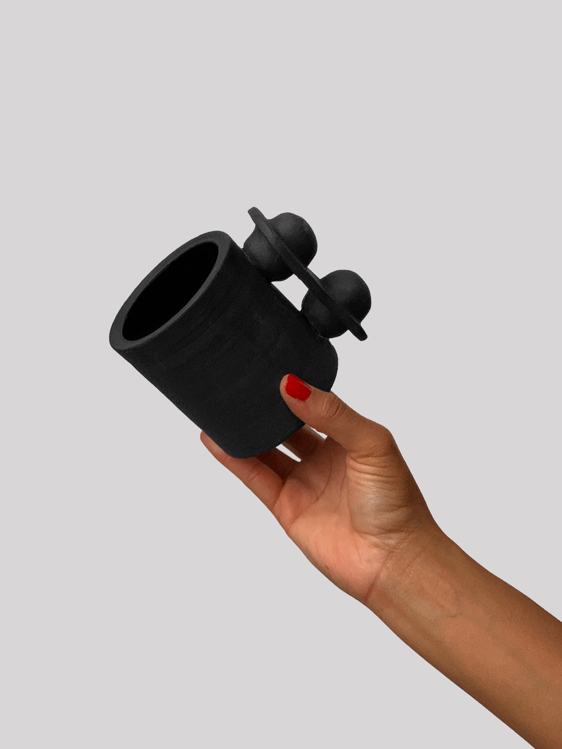 Black matte stoneware ceramic mug with an oval thin plate around two balls extending to the side of the mug as the handle.