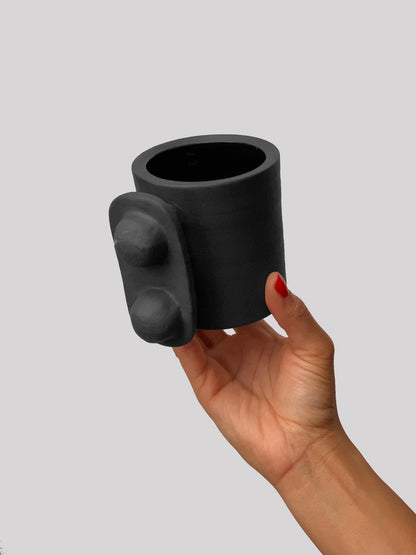 Black matte stoneware ceramic mug with an oval thin plate around two balls extending to the side of the mug as the handle.