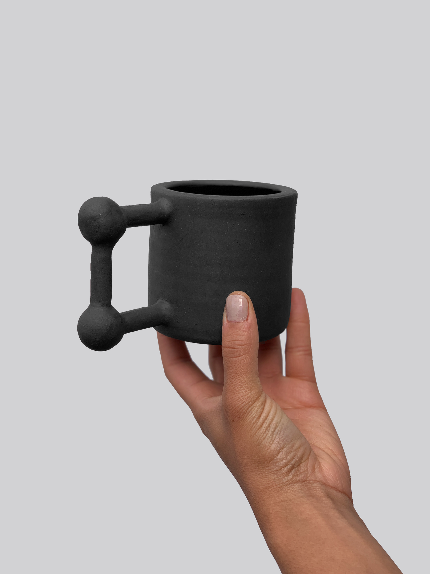 Black matte stoneware ceramic mug with a  square shape and ball accents on the corners of the handle.