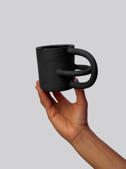 Black matte stoneware ceramic mug with intersecting arches as the handle.