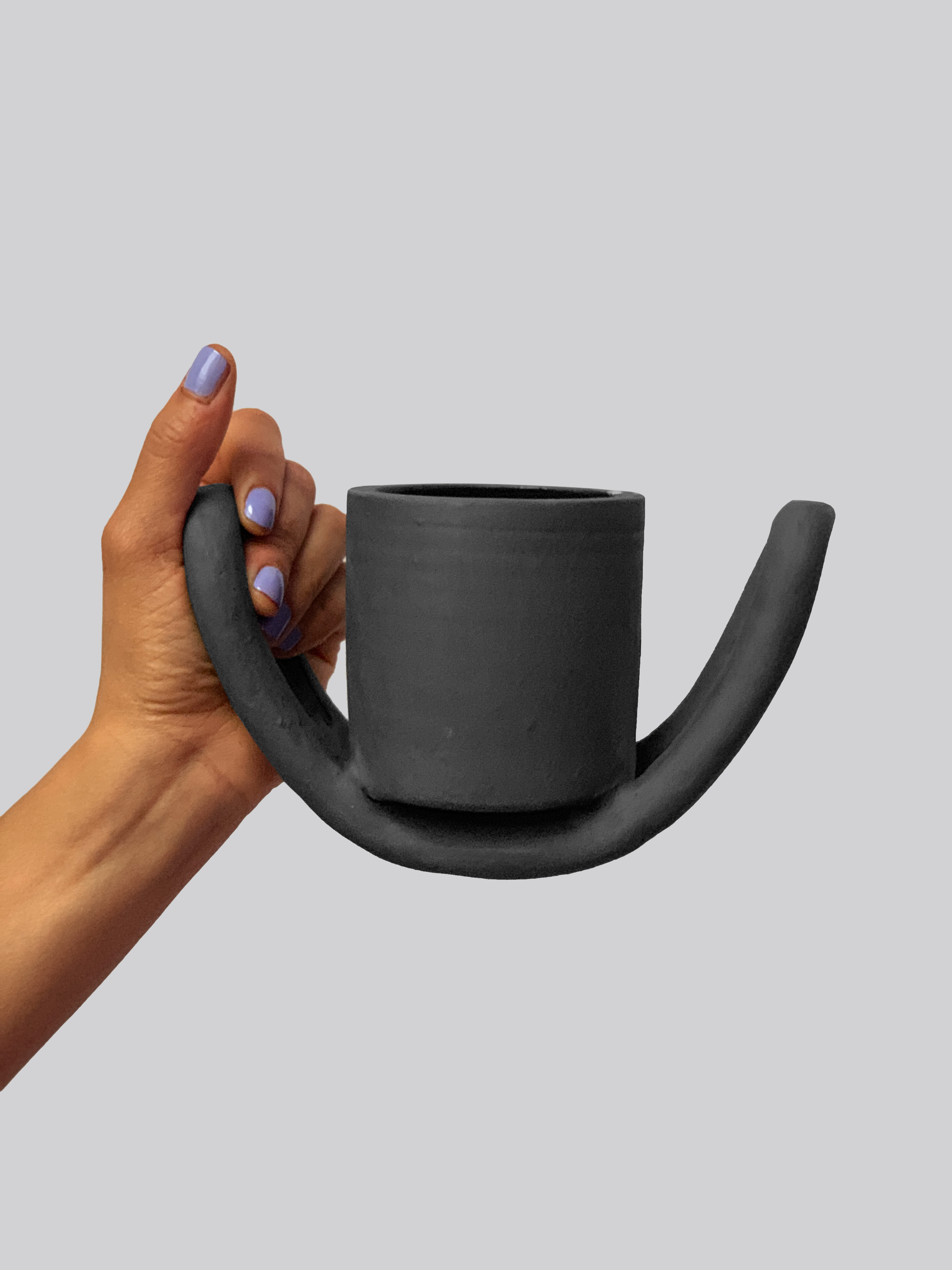 Black matte stoneware ceramic mug sitting on a half circle shaped figure as the handles. 