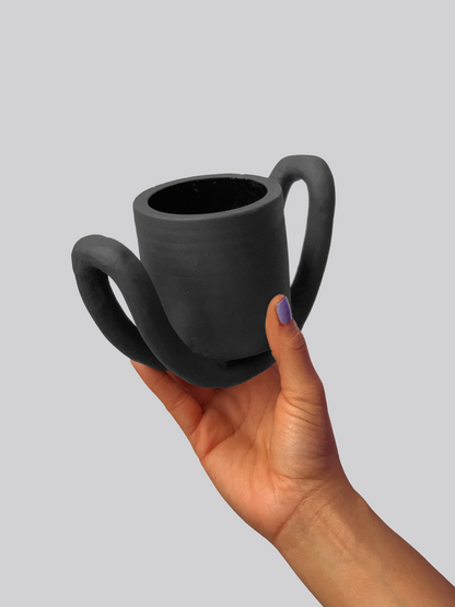 Black matte stoneware ceramic mug sitting on a half circle shaped figure as the handles.