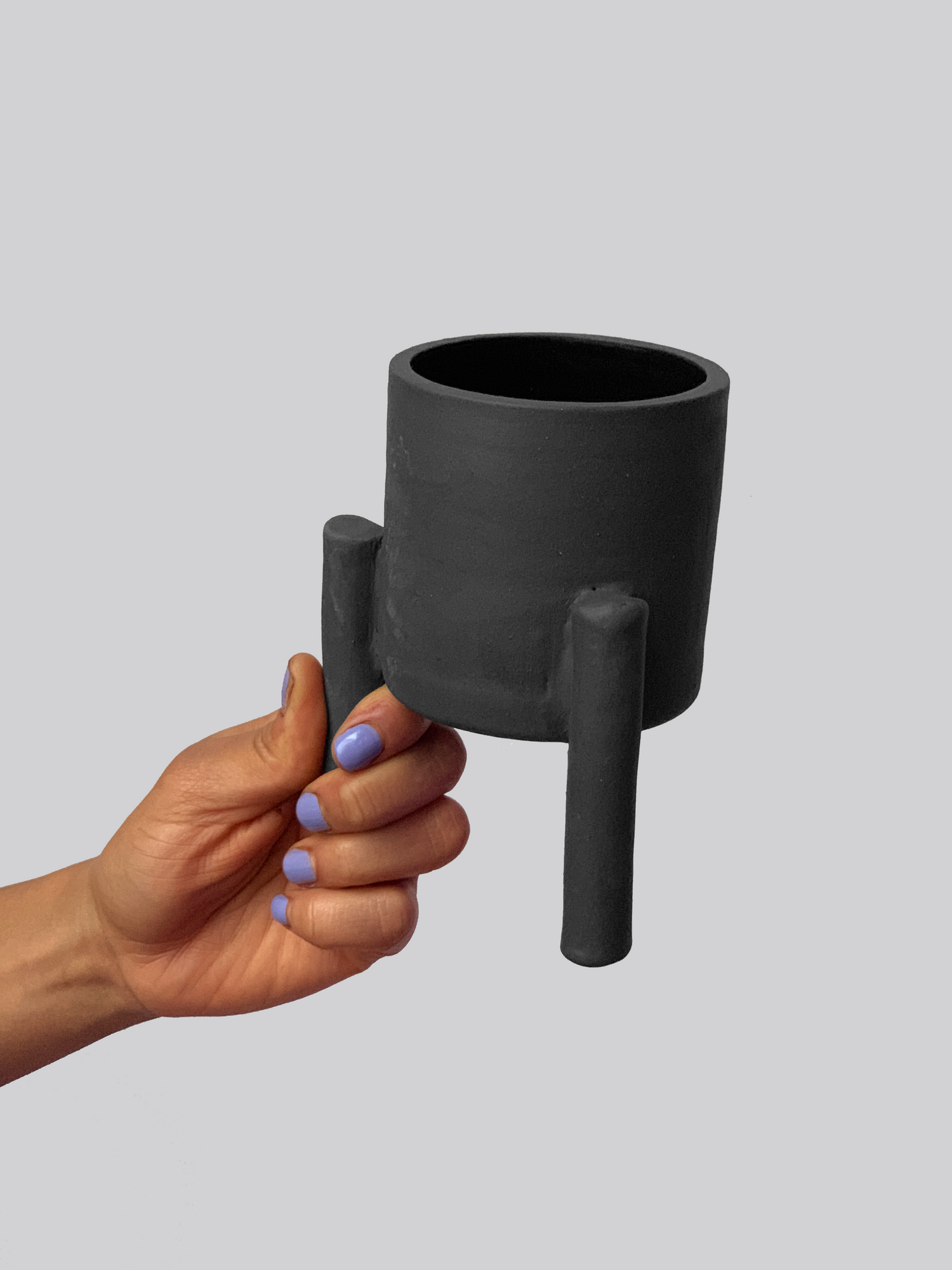Black matte stoneware ceramic mug with three legs as the handle.
