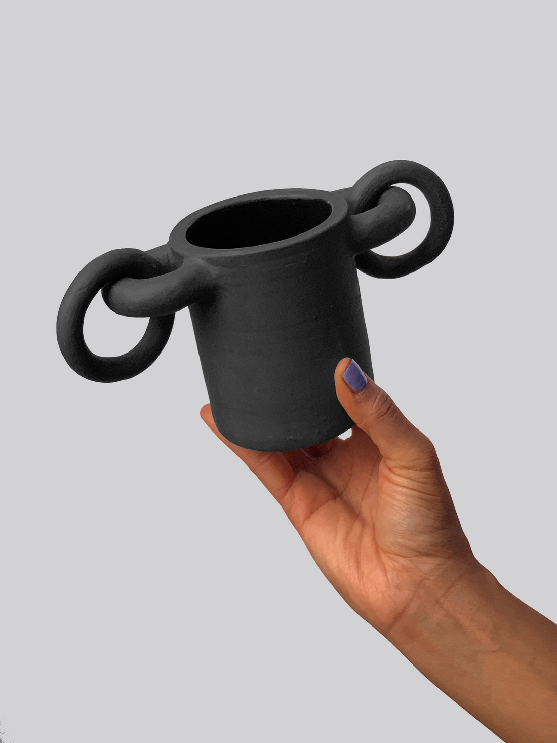 Black matte stoneware ceramic mug with circular shapes on both sides of the mug and rings passing through them as the handle. 