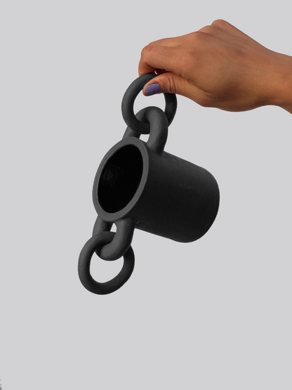 Black matte stoneware ceramic mug with circular shapes on both sides of the mug and rings passing through them as the handle.