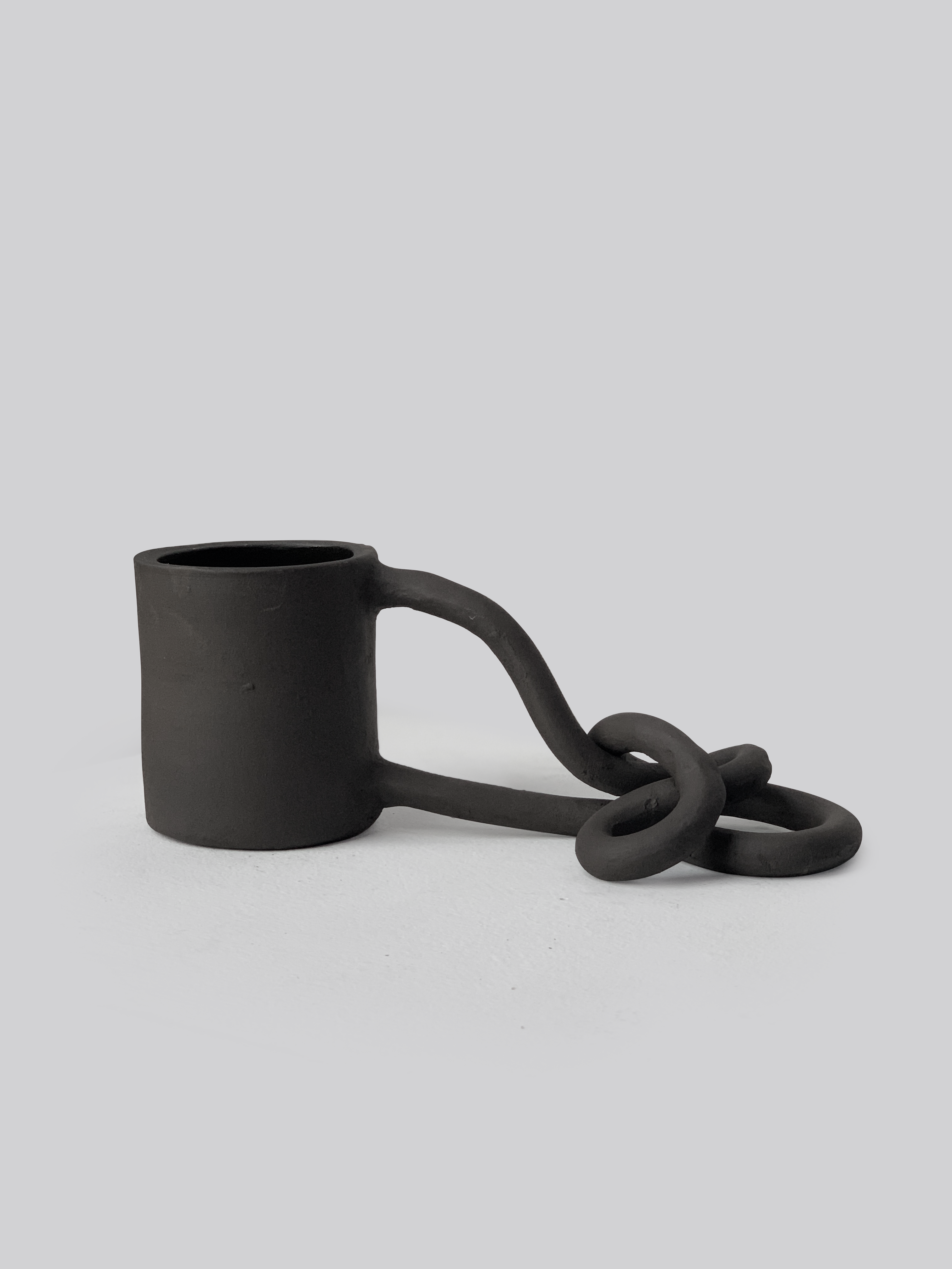Black matte stoneware ceramic mug with a handle that flows down and loops around itself and rests on a surface.
