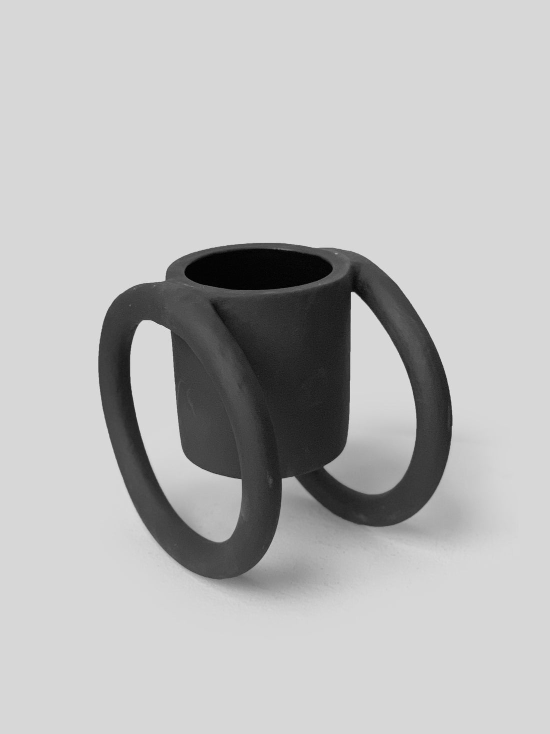 Black matte stoneware ceramic mug suspended from a circular disc on each side of the mug as the handles.