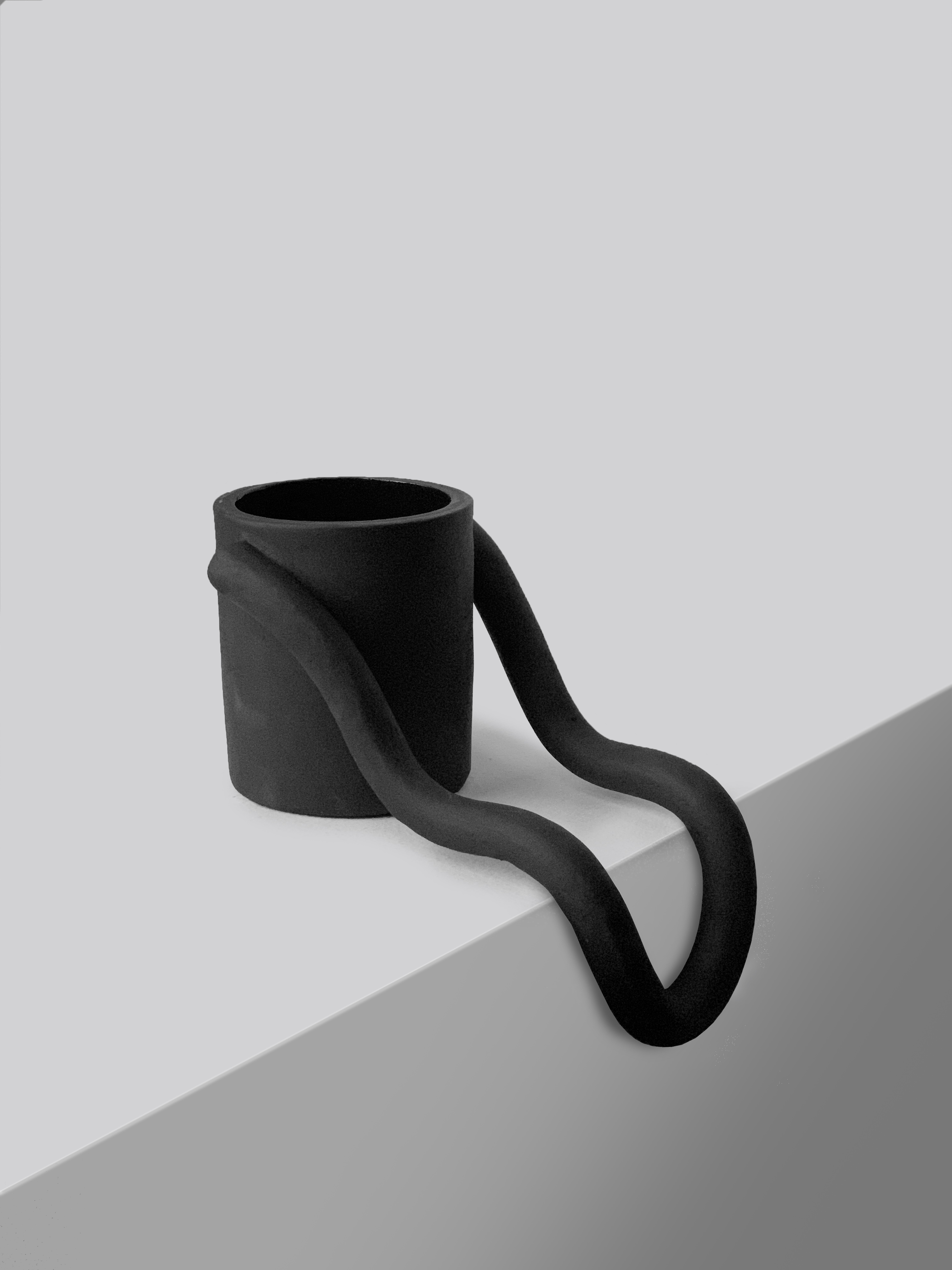 Black matte stoneware ceramic mug with a handle that flows down the side of a surface. 