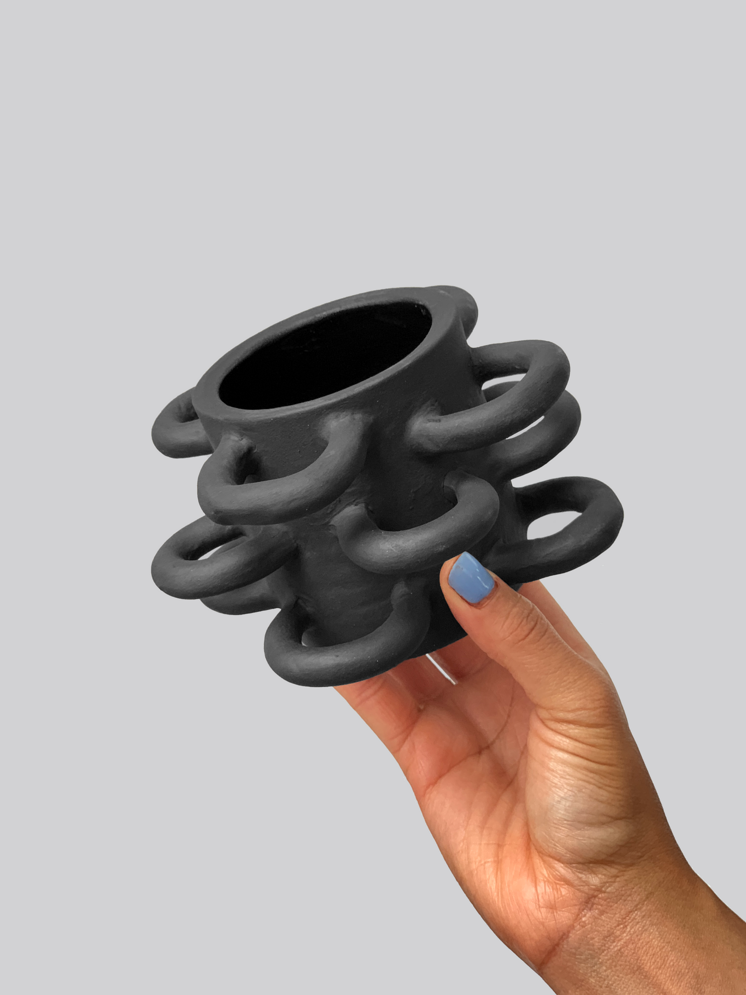 Black matte stoneware ceramic mug with half circle shapes throughout the exterior of the mug as the handles. 