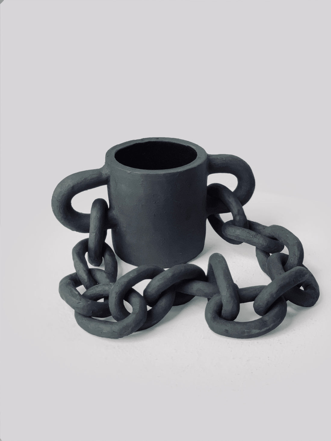 Black matte stoneware ceramic mug with a half shaped oval on each side of the mug and oval link chain passing through as the handle.