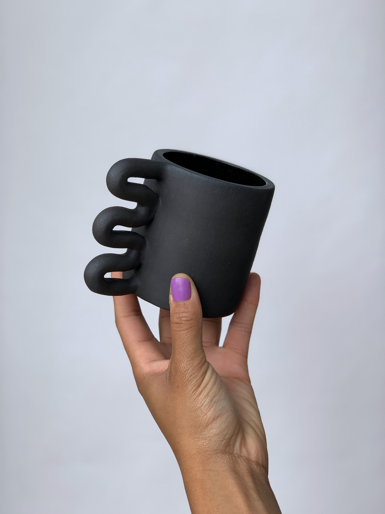 Black matte stoneware ceramic mug with a squiggle shaped handle.