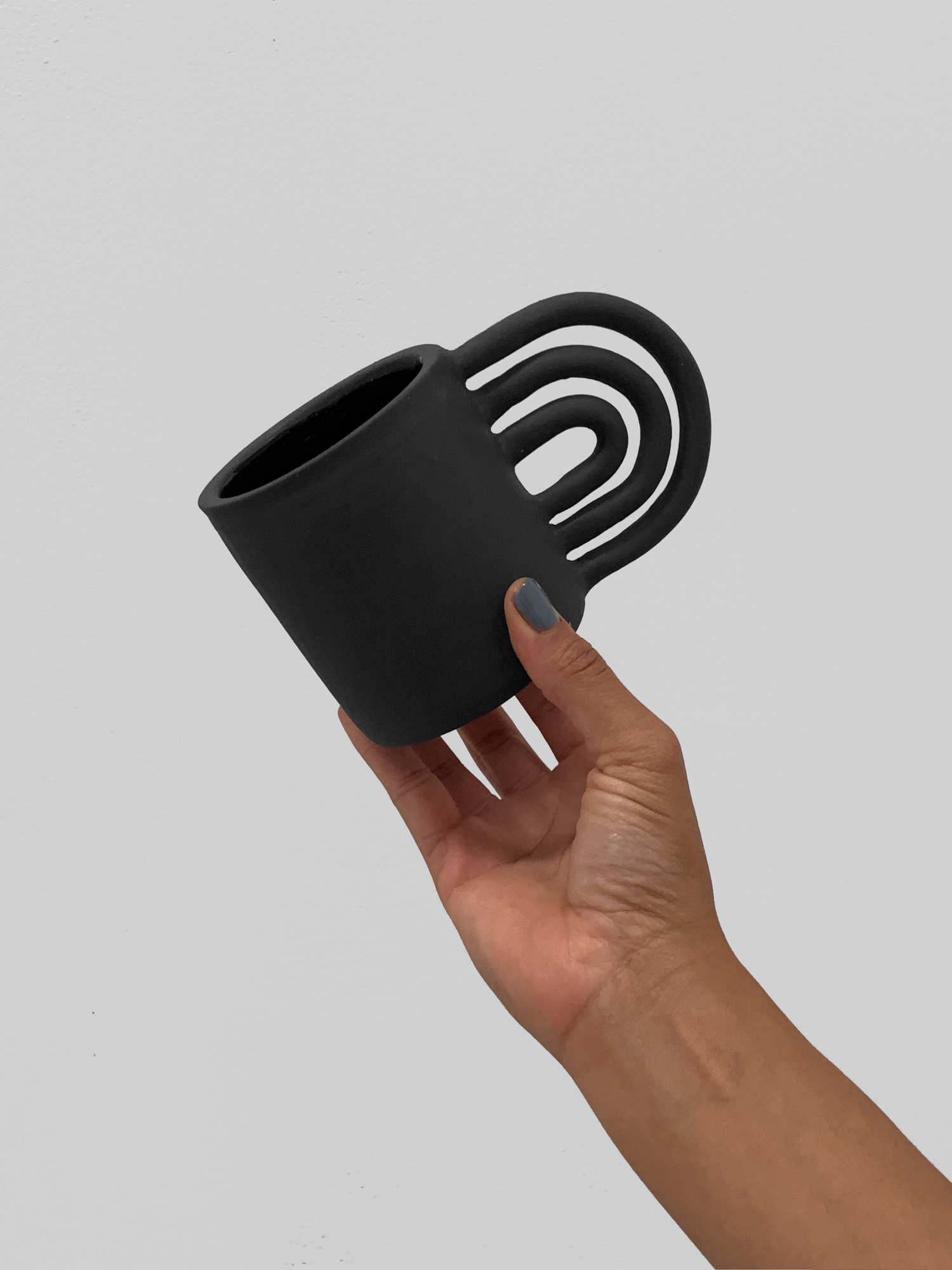 Black matte stoneware ceramic mug with a rainbow shaped handle.