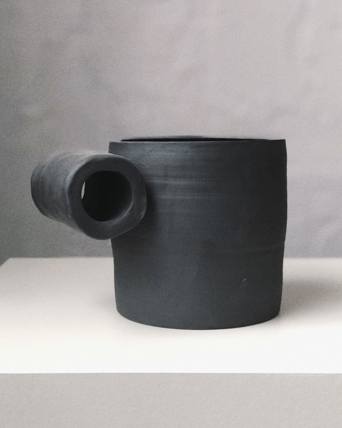 Black matte stoneware ceramic mug with a full side roll as the handle.