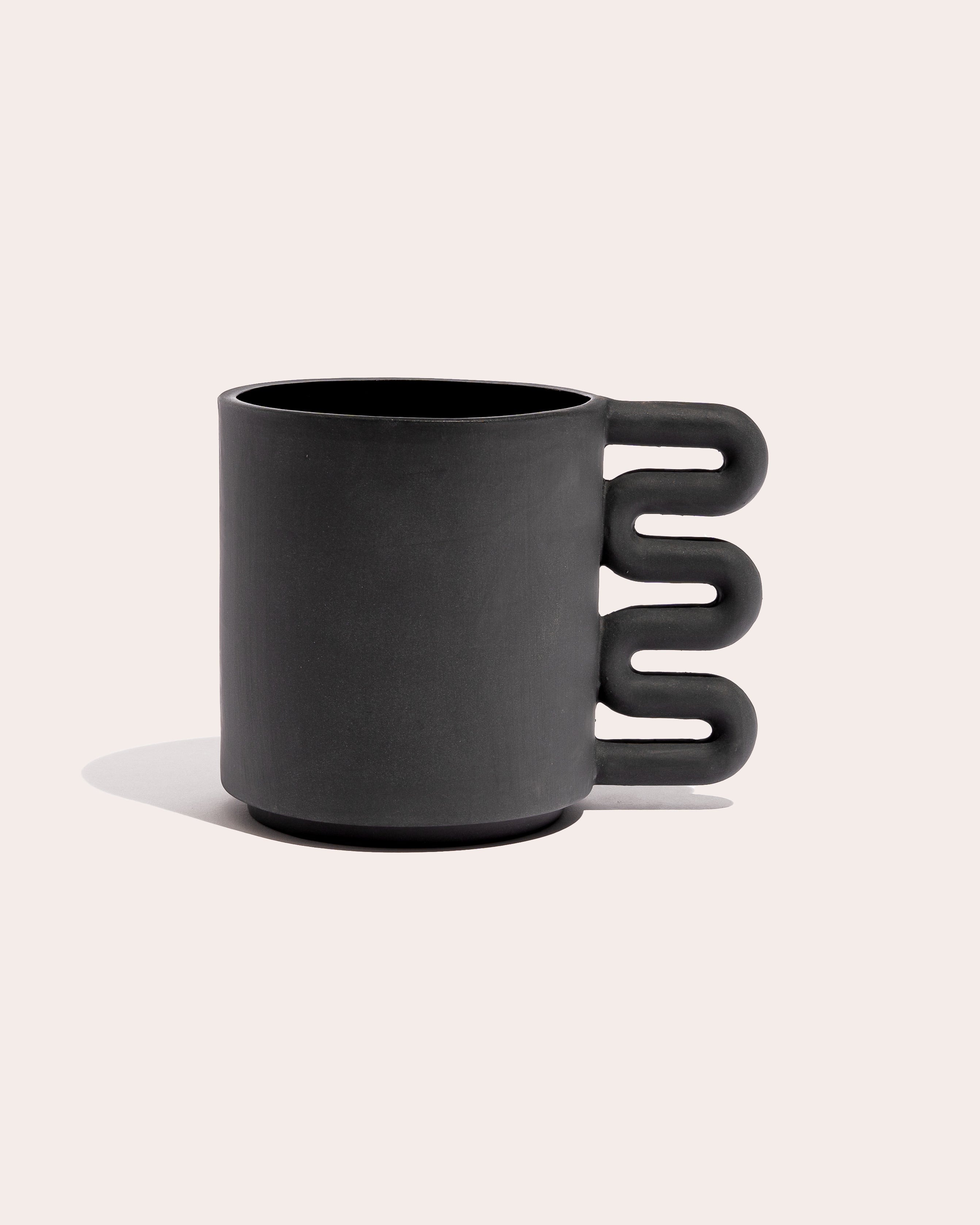 Black matte stoneware ceramic mug with a squiggle shaped handle.