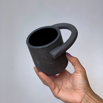 Black matte stoneware ceramic mug with a circular handle extending outwards to the side of the mug as the handle.